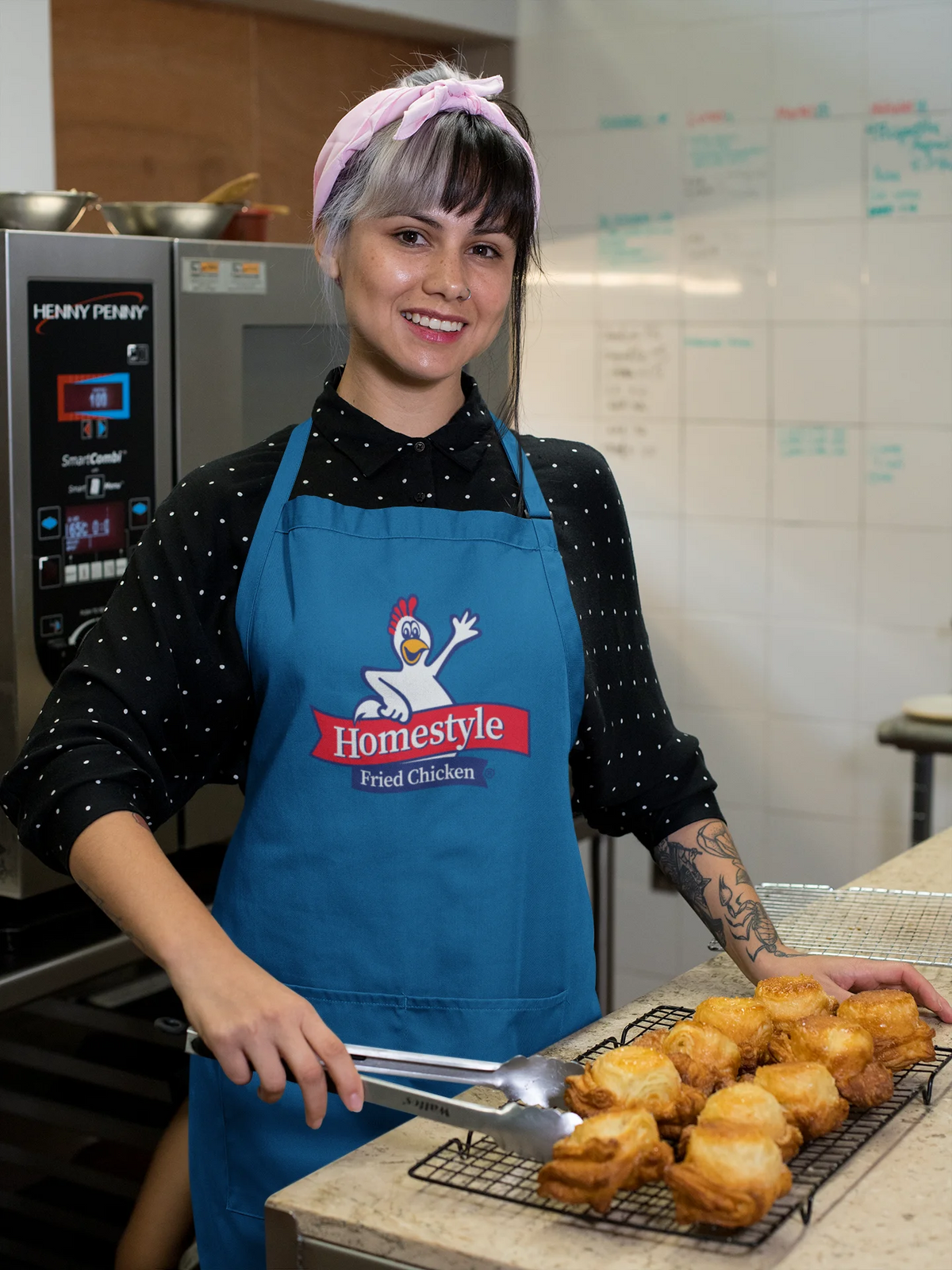Person wearing a blue apron with a Homestyle Fried Chicken logo, standing behind a counter with fried chicken.